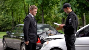 A man wonders if he needs a police report to file an insurance claim as he speaks with a police officer after a car accident.